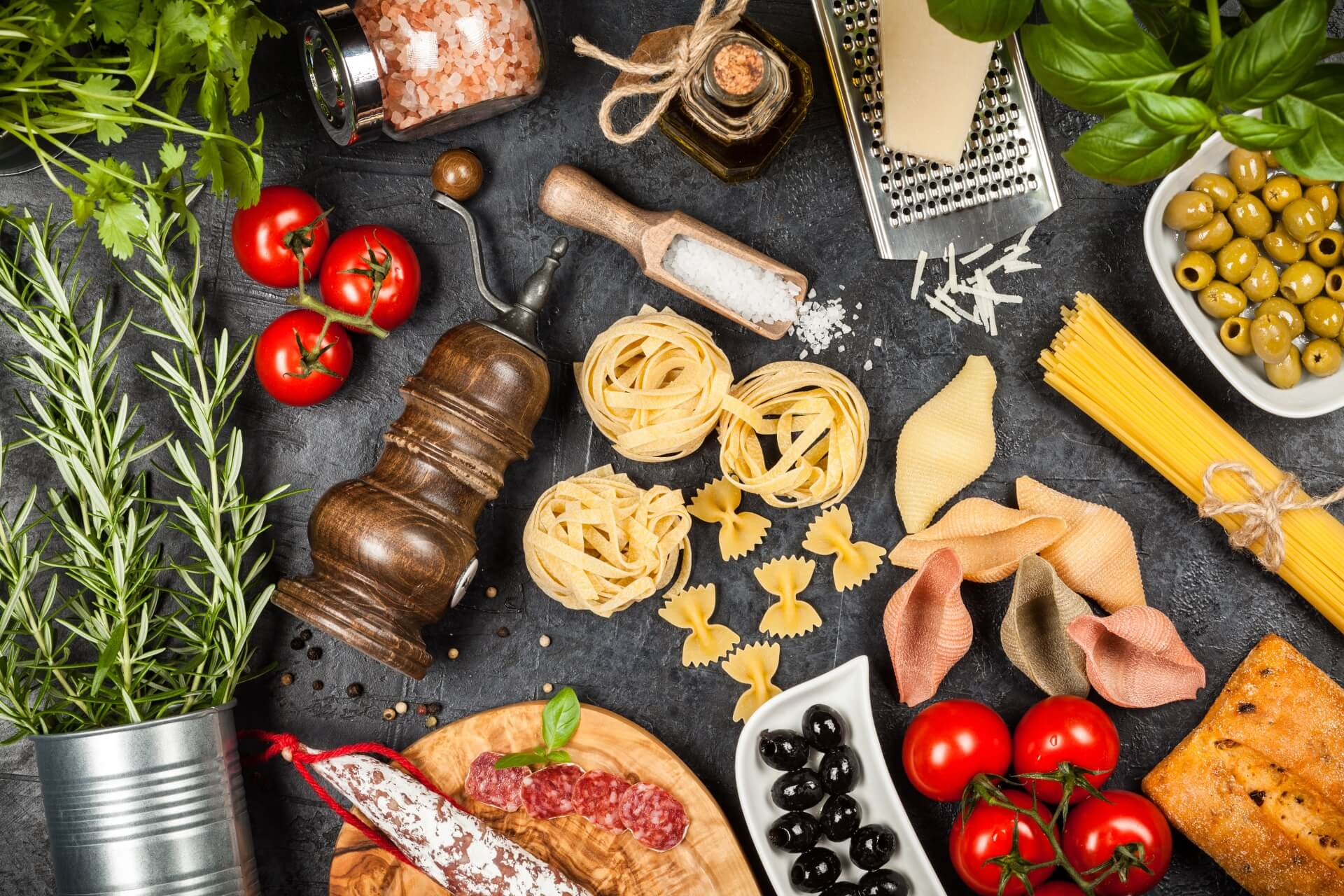 Italienische Delikatessen: Ausgewählte Zutaten wie Pasta, Salami, Oliven, Kräuter, Tomaten, Parmesan und Olivenöl – hochwertige Lebensmittel für echte italienische Küche.